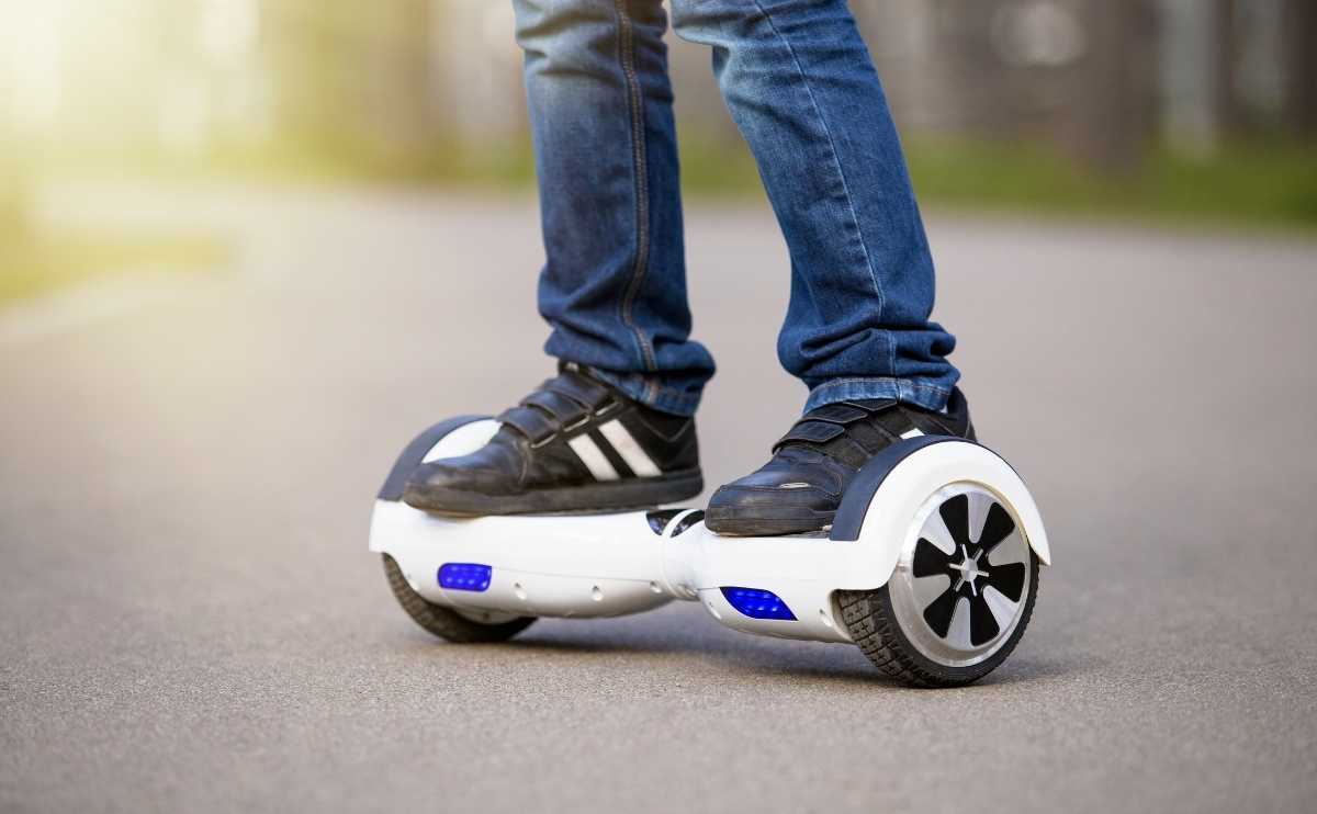 Kid's feet up close riding on a hoverboard outside.