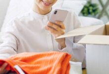 Woman looking at an opened clothing subscription box and taking a photo of clothes