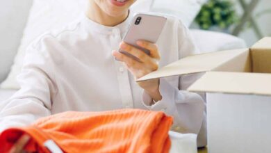 Woman looking at an opened clothing subscription box and taking a photo of clothes